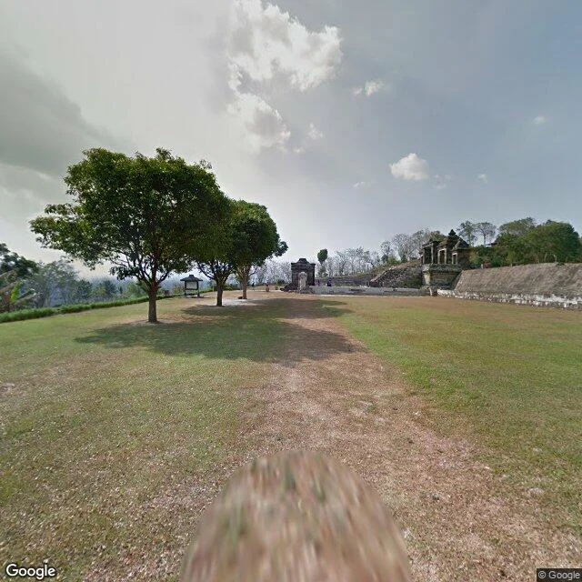 A hilltop of grass: three trees in a row, a dirt path, and weathered stone gates at the far edge against the haze. Street view, July 2015.